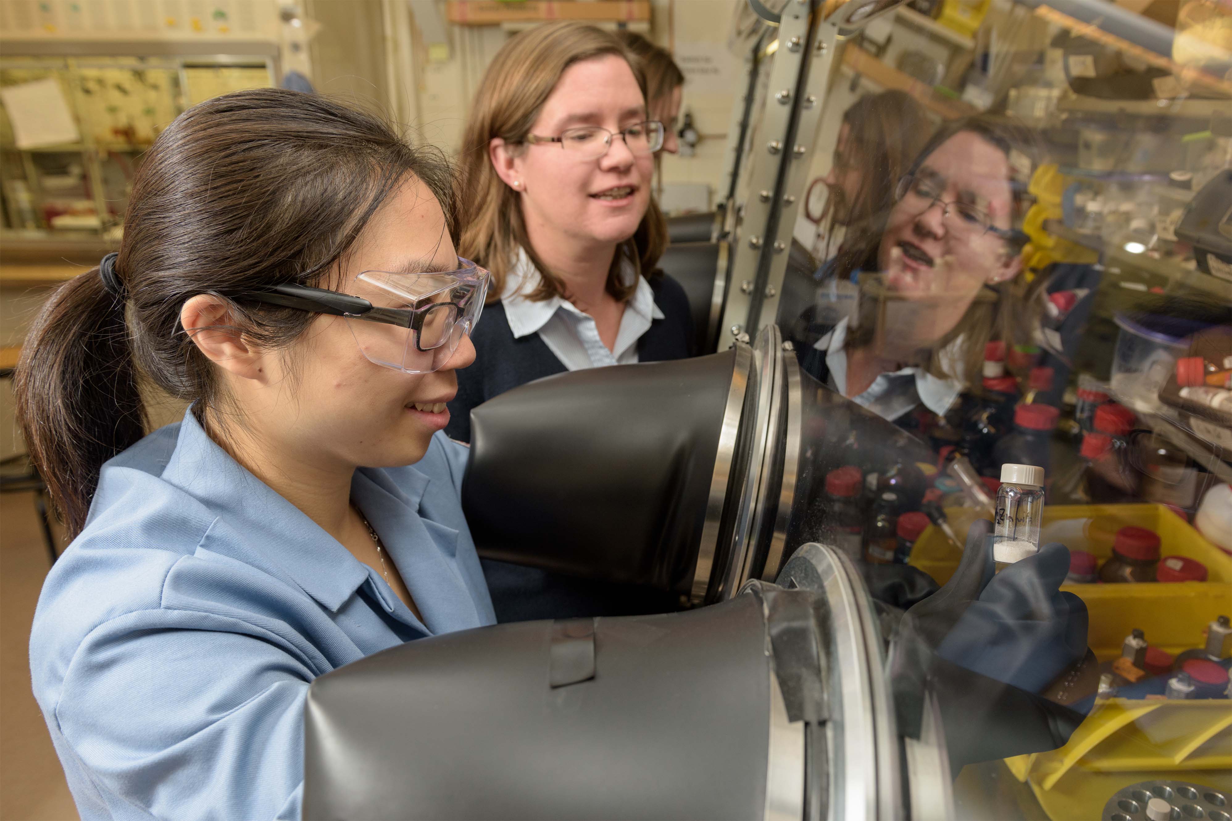 Faculty member directs graduate student as she conducts experiment inside a vent hood. 